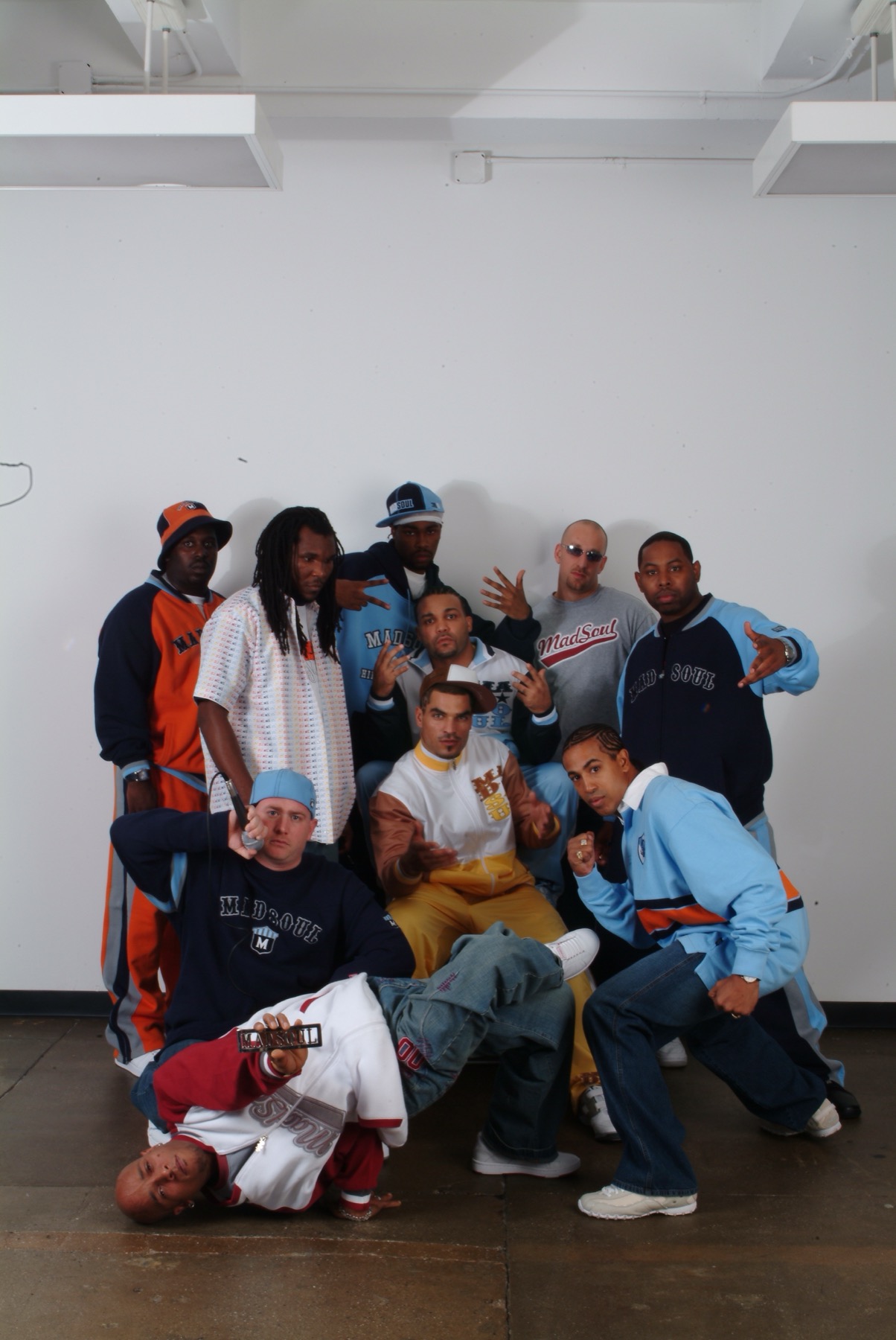 Ten real Madsoul models and crew posing together in a loft space, most wearing real Madsoul-branded jackets, hoodies and tees, one doing a b-boy floor freeze in front