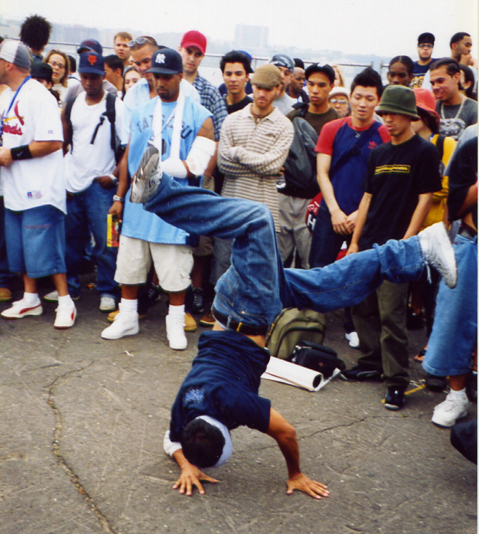A b-boy mid-freeze in a street cypher on a New York rooftop, a crowd watching, real Madsoul marketing photography